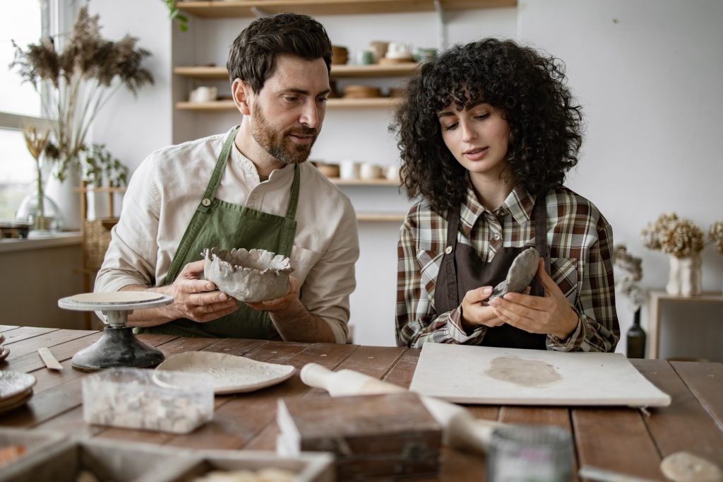 Bearded man and woman sculpting clay pottery together in art studio