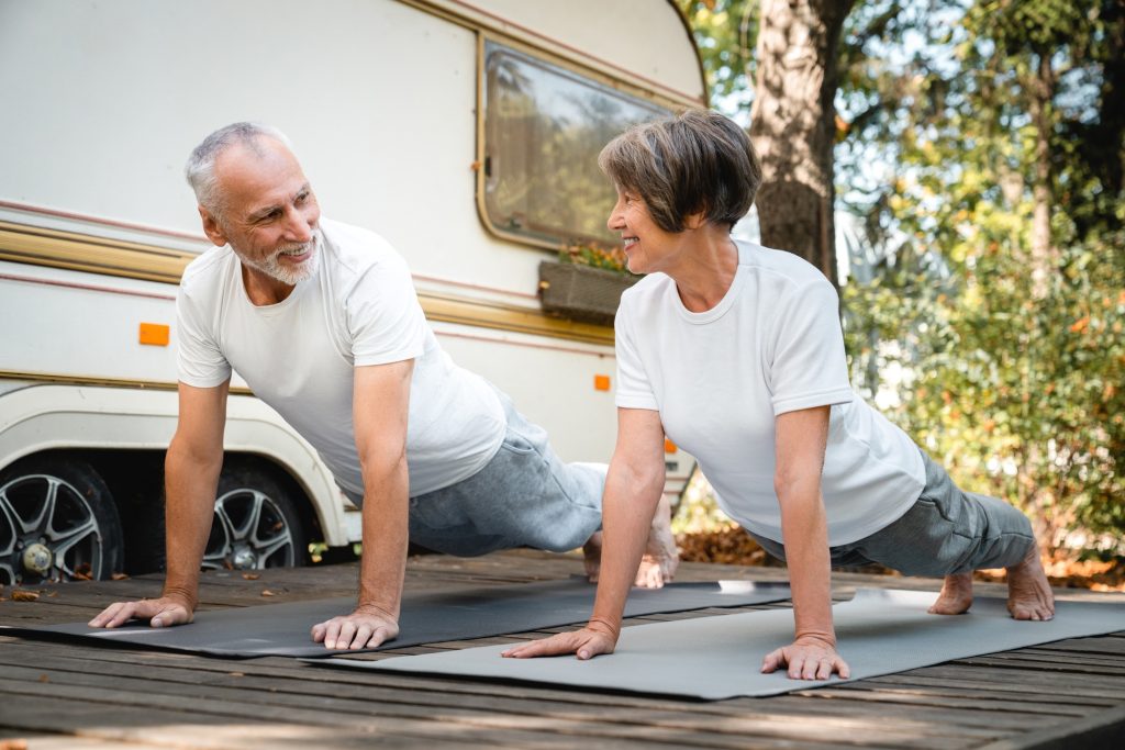 Grandparents doing sporty activity on fitness mats, slimming together while on a trip in trailer