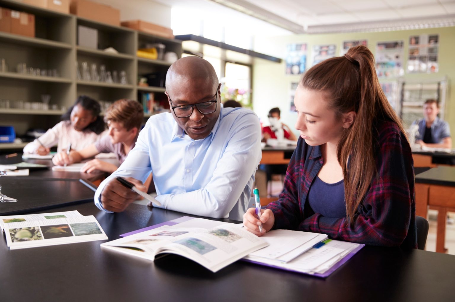 High School Tutor Sitting At Desk With Female Student In Biology Class
