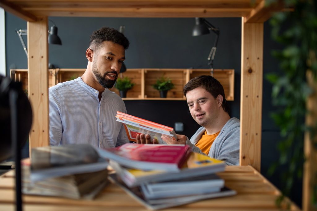 Young happy man with Down syndrome and his tutor indoors at staffroom